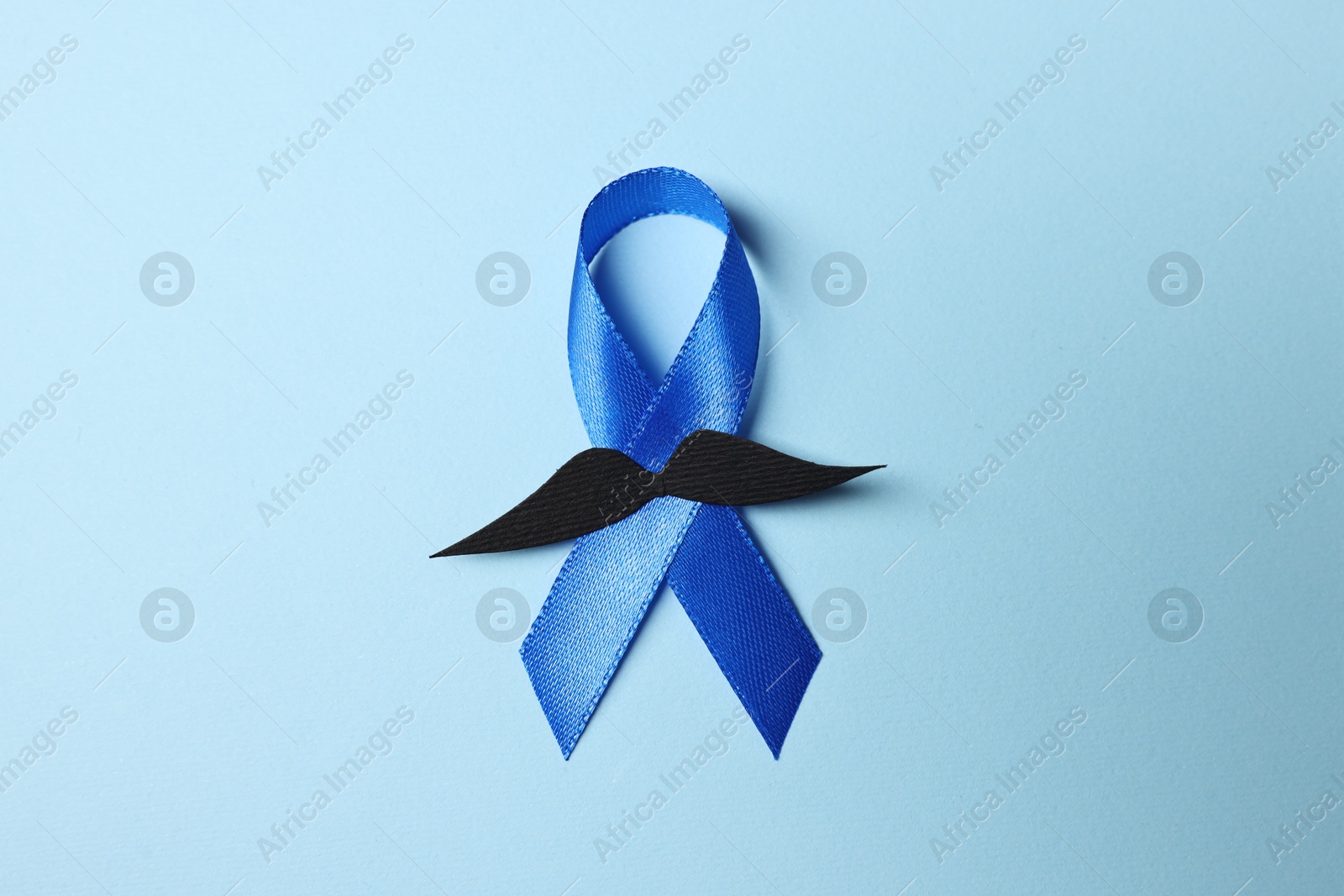 Photo of Blue ribbon and fake mustache on light background, top view. Prostate cancer awareness