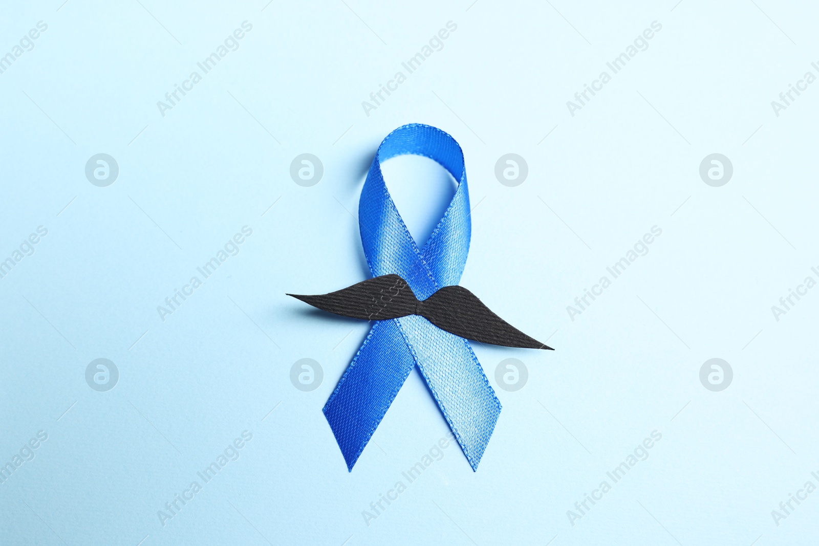 Photo of Blue ribbon and fake mustache on light background, top view. Prostate cancer awareness