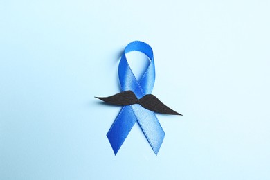 Photo of Blue ribbon and fake mustache on light background, top view. Prostate cancer awareness