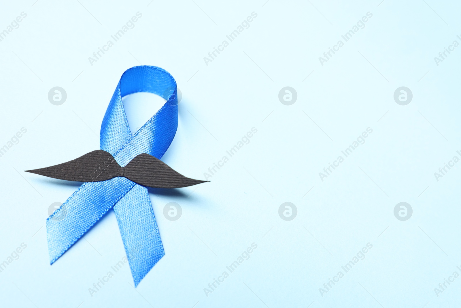 Photo of Blue ribbon and fake mustache on light background, space for text. Prostate cancer awareness