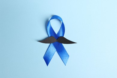 Photo of Blue ribbon and fake mustache on light background, top view. Prostate cancer awareness