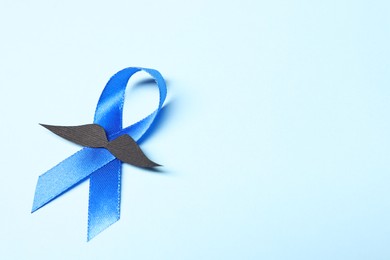 Photo of Blue ribbon and fake mustache on light background, space for text. Prostate cancer awareness