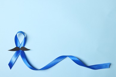 Photo of Blue ribbon and fake mustache on light background, top view with space for text. Prostate cancer awareness