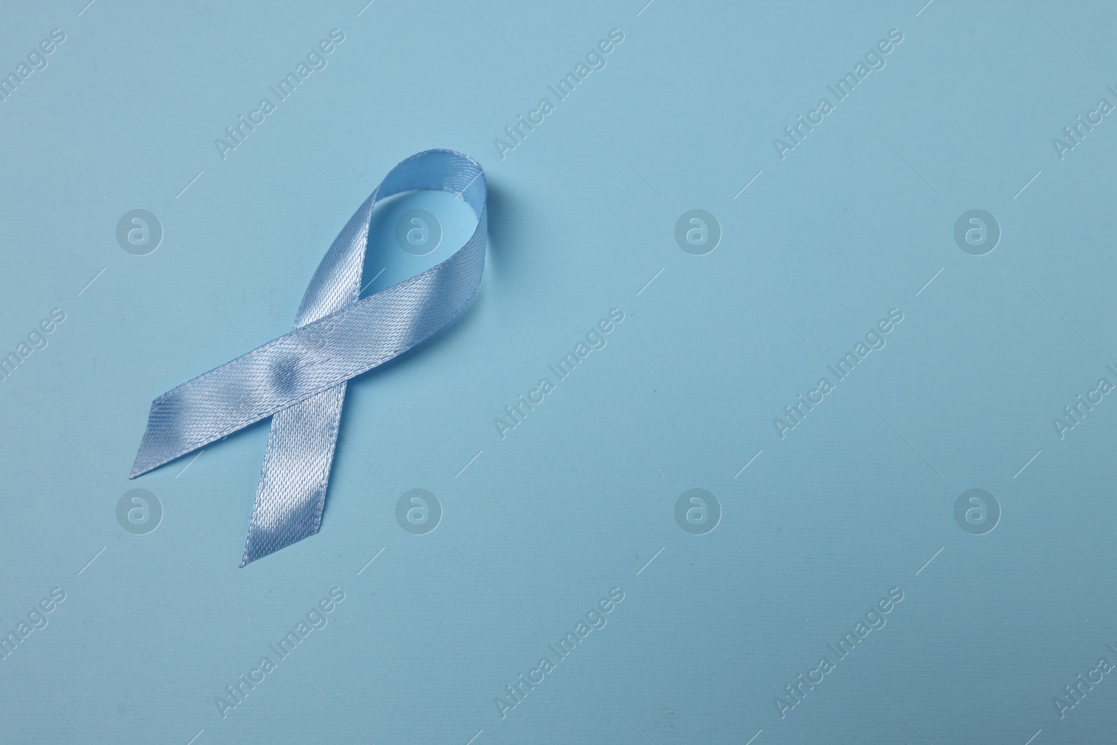 Photo of Light blue ribbon on color background, top view with space for text. Prostate cancer awareness