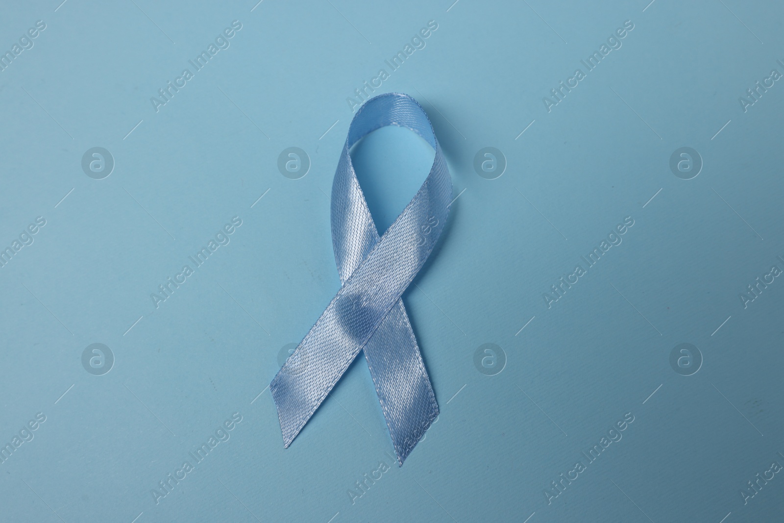 Photo of Light blue ribbon on color background, top view. Prostate cancer awareness