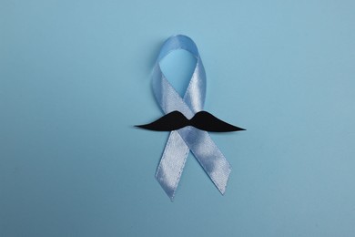 Photo of Light blue ribbon and fake mustache on color background, top view. Prostate cancer awareness