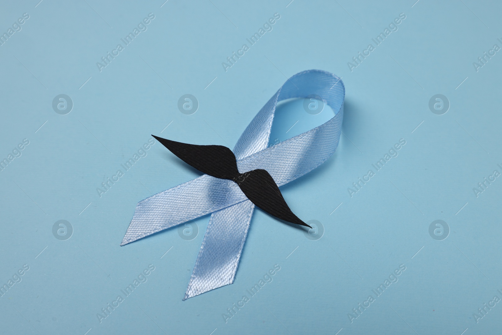 Photo of Light blue ribbon and fake mustache on color background, closeup. Prostate cancer awareness