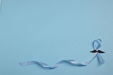 Photo of Light blue ribbon and fake mustache on color background, top view with space for text. Prostate cancer awareness