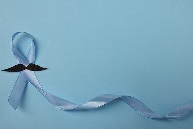 Photo of Light blue ribbon and fake mustache on color background, top view with space for text. Prostate cancer awareness