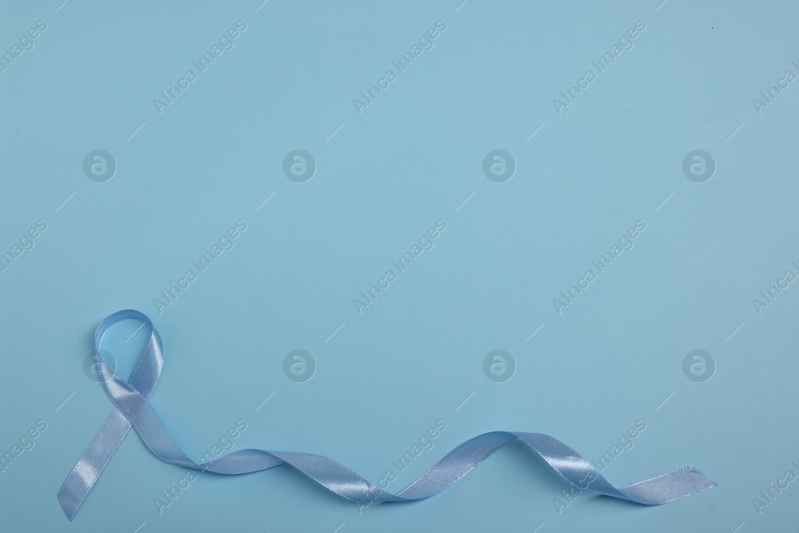 Photo of Light blue ribbon on color background, top view with space for text. Prostate cancer awareness