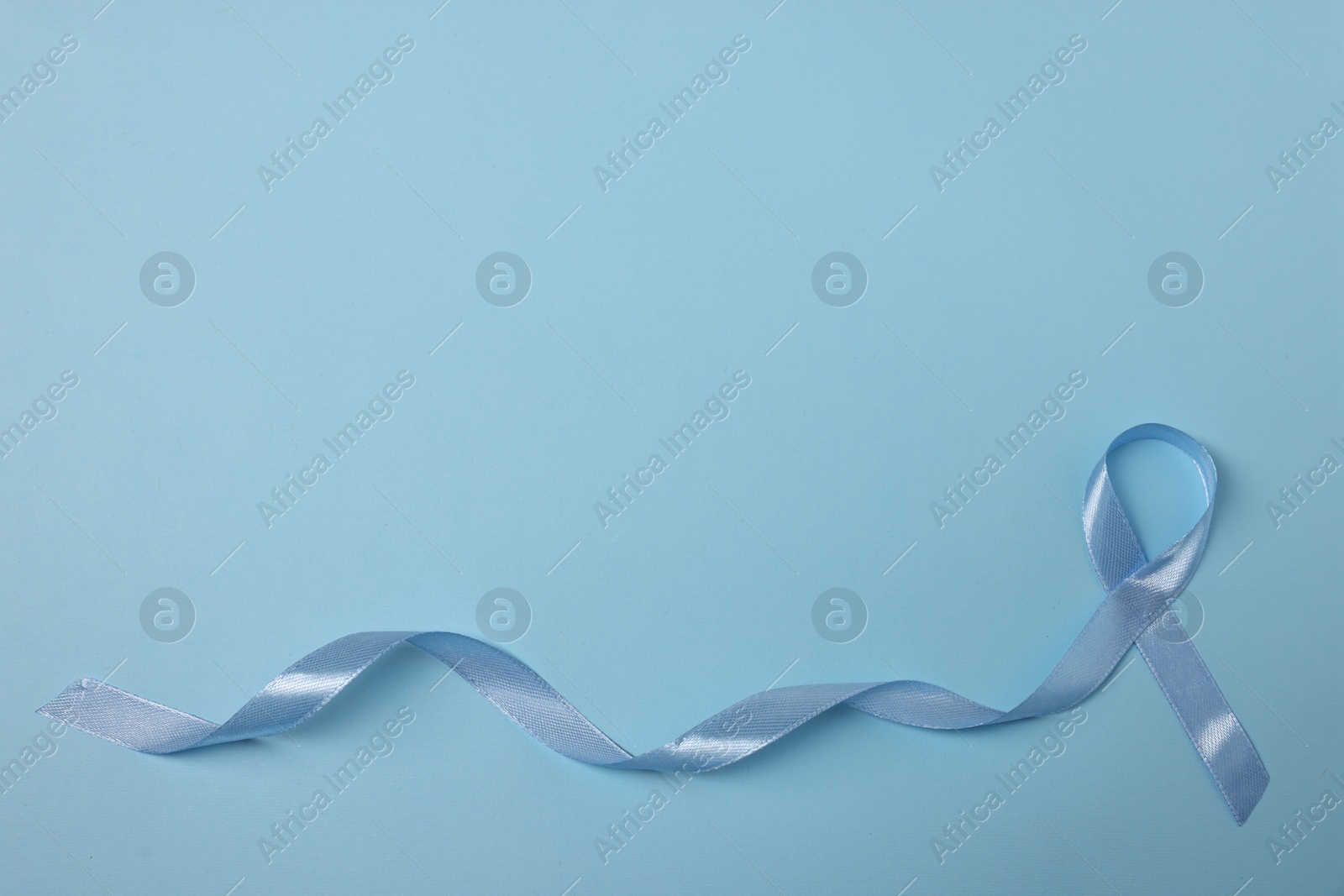 Photo of Light blue ribbon on color background, top view with space for text. Prostate cancer awareness