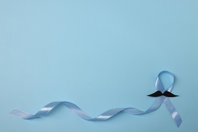 Photo of Light blue ribbon and fake mustache on color background, top view with space for text. Prostate cancer awareness