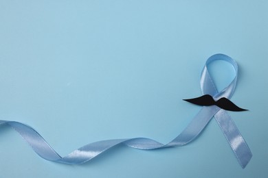 Photo of Light blue ribbon and fake mustache on color background, top view with space for text. Prostate cancer awareness