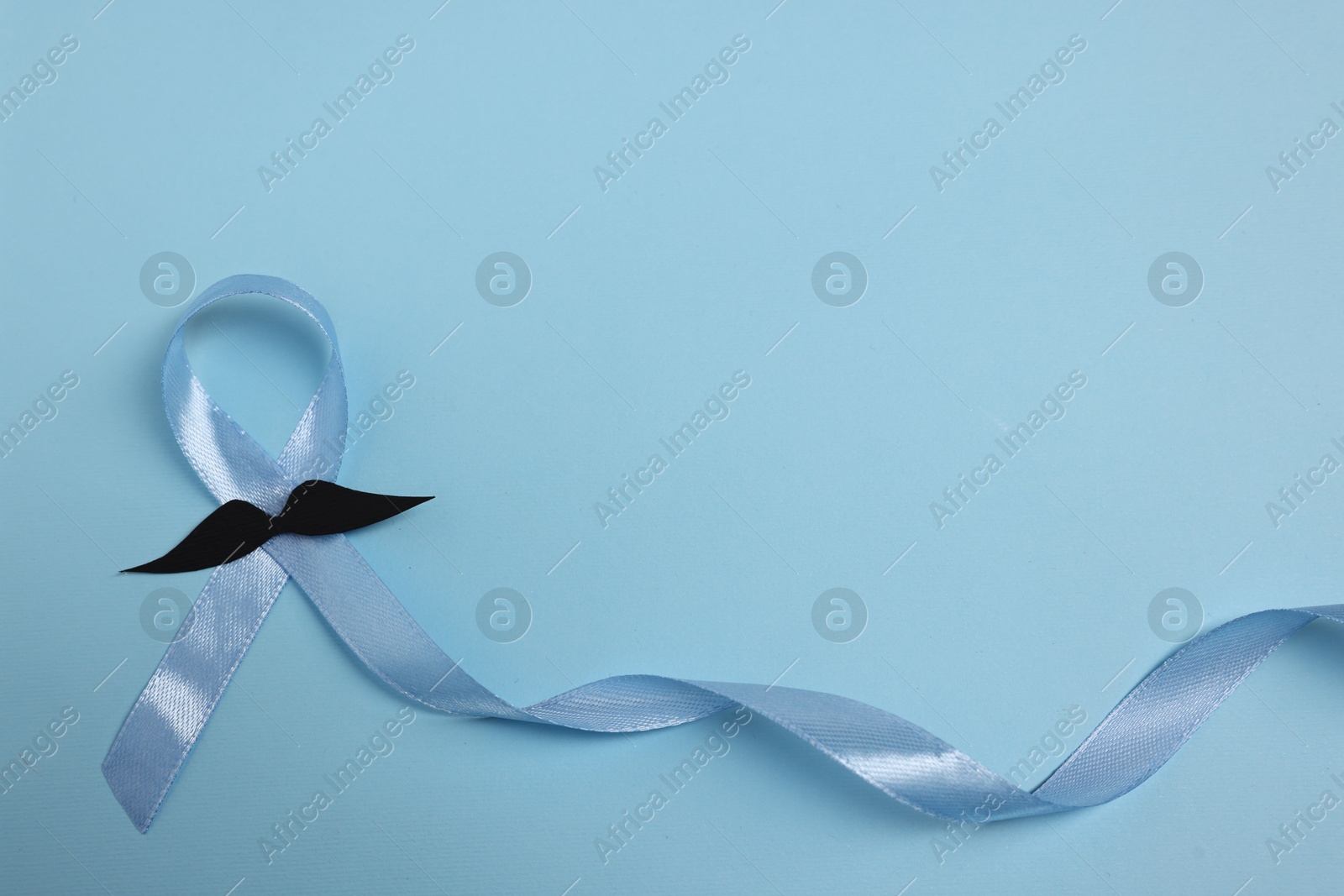 Photo of Light blue ribbon and fake mustache on color background, top view with space for text. Prostate cancer awareness