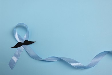 Photo of Light blue ribbon and fake mustache on color background, top view with space for text. Prostate cancer awareness