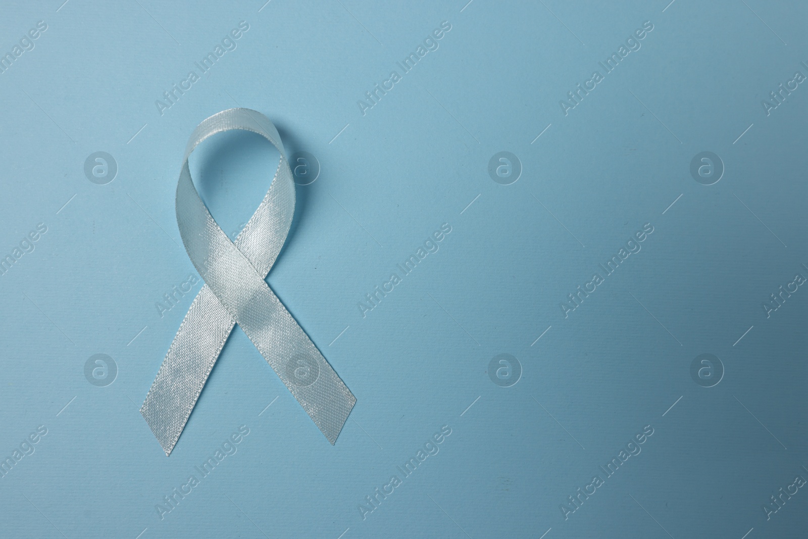 Photo of Light blue ribbon on color background, top view with space for text. Prostate cancer awareness