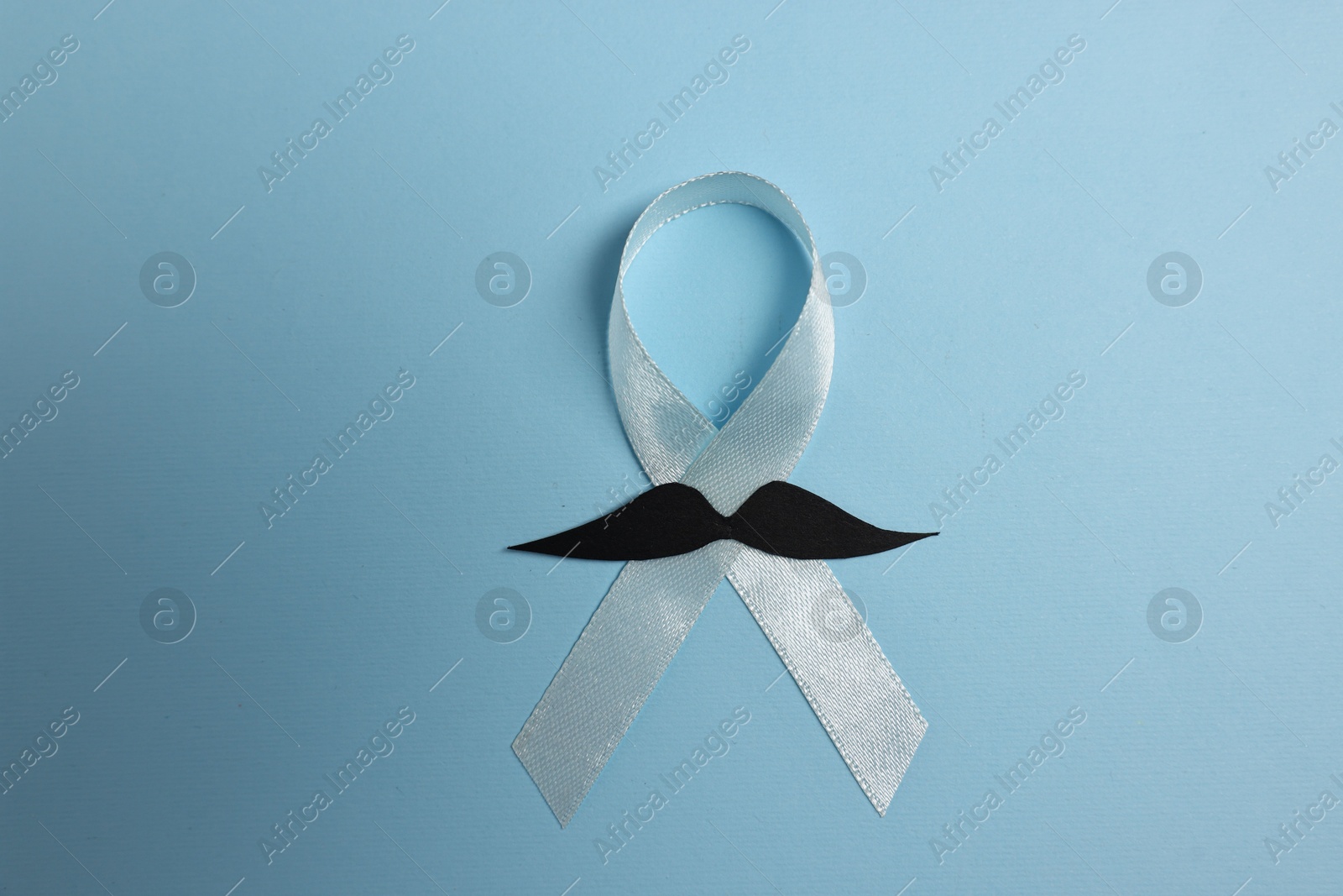 Photo of Light blue ribbon and fake mustache on color background, top view. Prostate cancer awareness