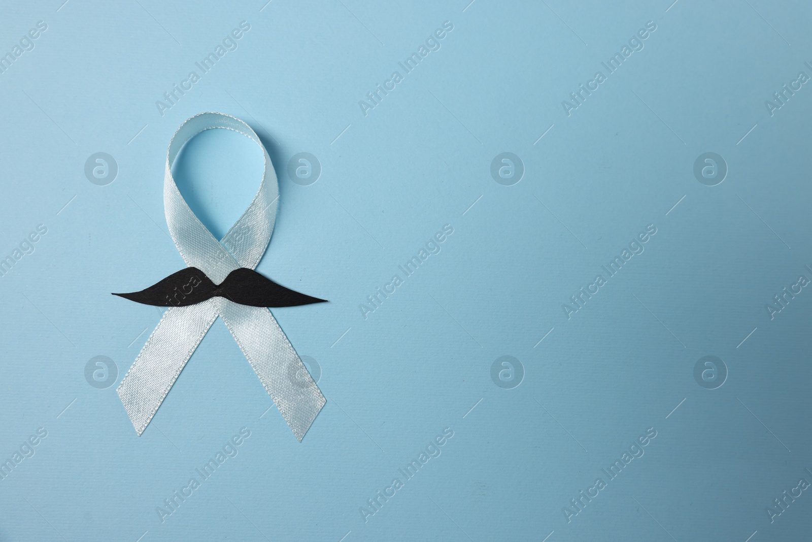 Photo of Light blue ribbon and fake mustache on color background, top view with space for text. Prostate cancer awareness