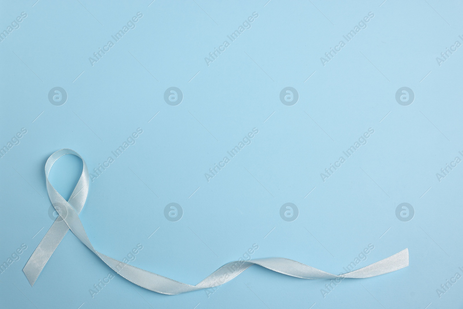 Photo of Light blue ribbon on color background, top view with space for text. Prostate cancer awareness