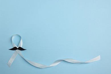 Photo of Light blue ribbon and fake mustache on color background, top view with space for text. Prostate cancer awareness