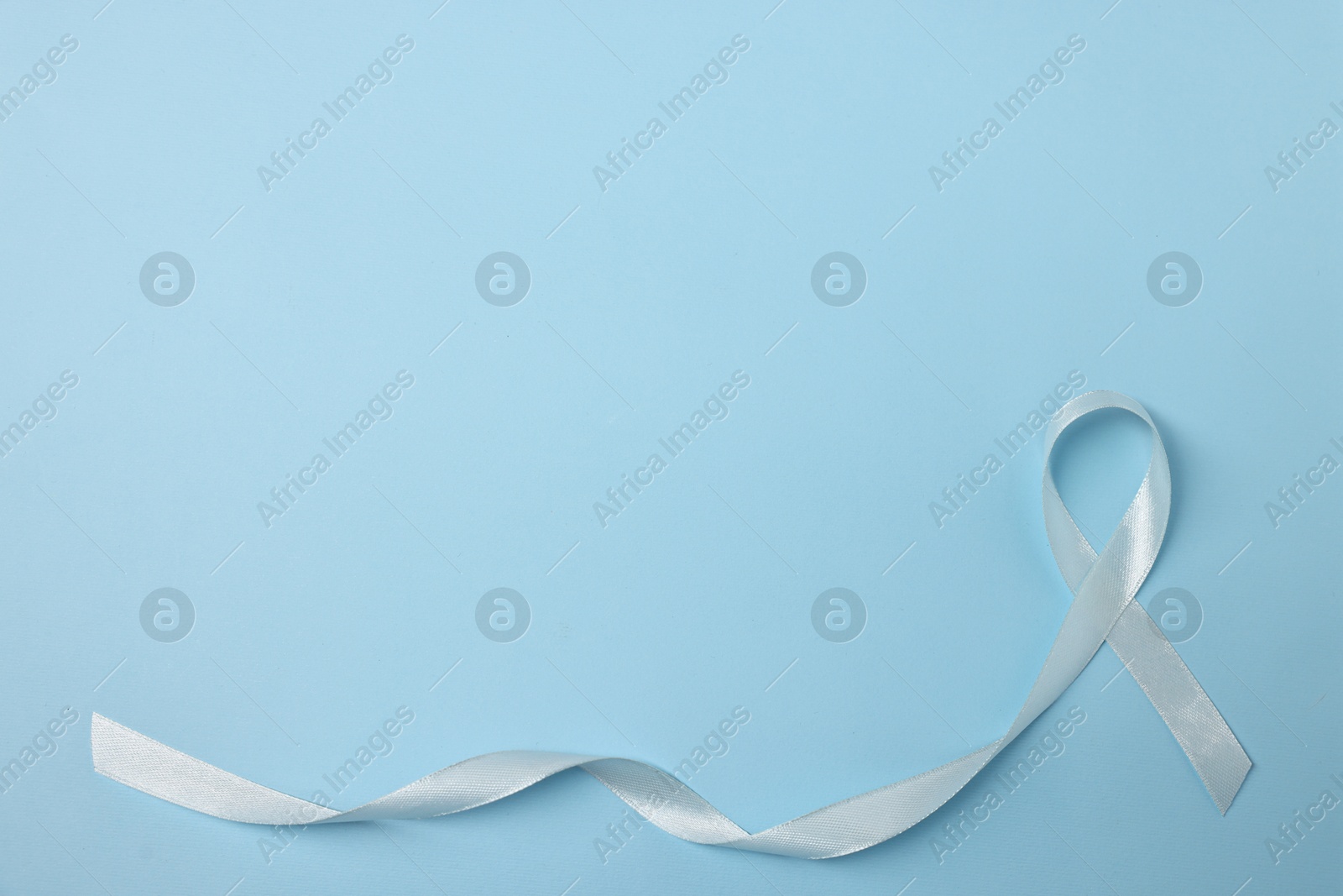 Photo of Light blue ribbon on color background, top view with space for text. Prostate cancer awareness