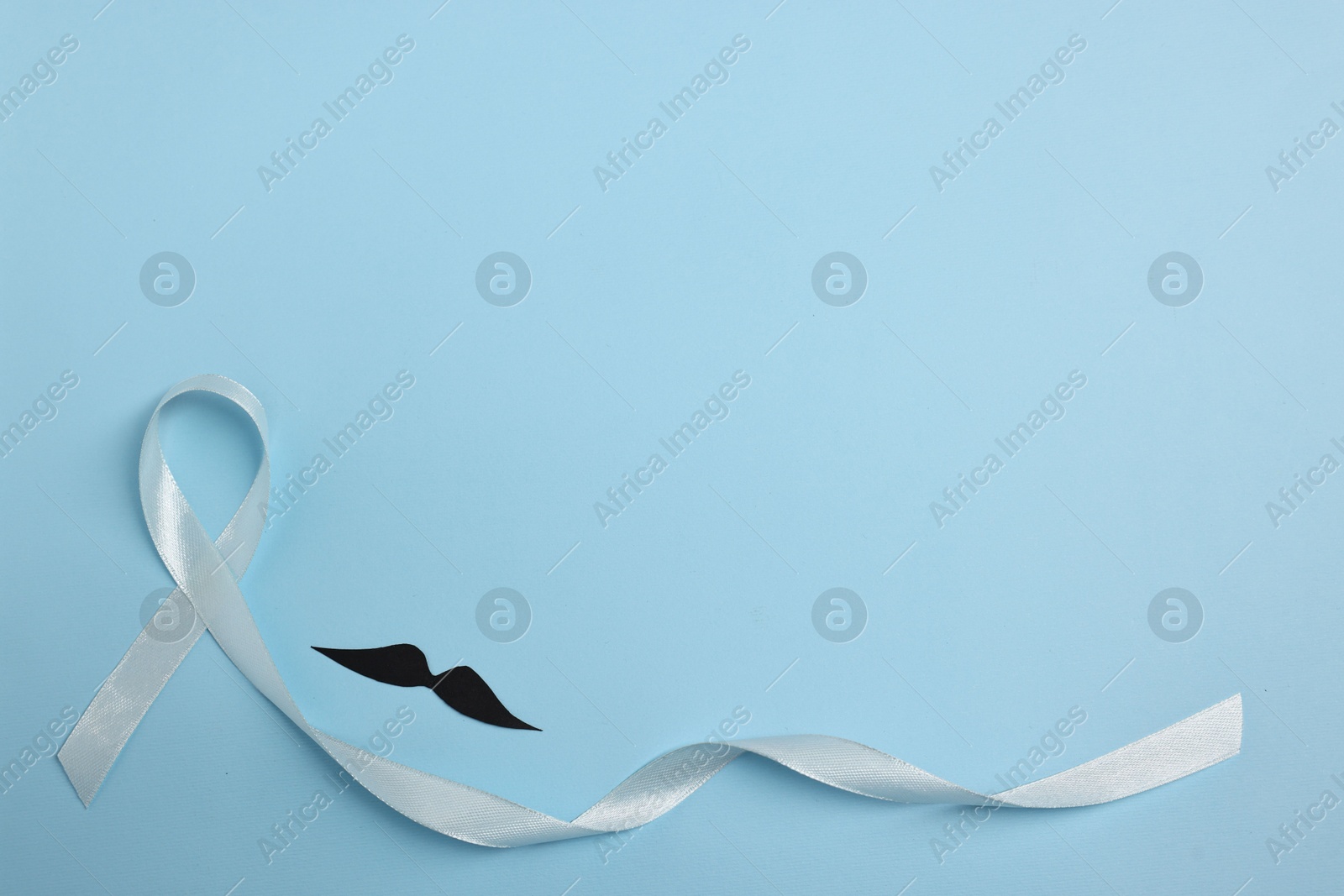 Photo of Light blue ribbon and fake mustache on color background, top view with space for text. Prostate cancer awareness