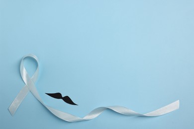 Photo of Light blue ribbon and fake mustache on color background, top view with space for text. Prostate cancer awareness