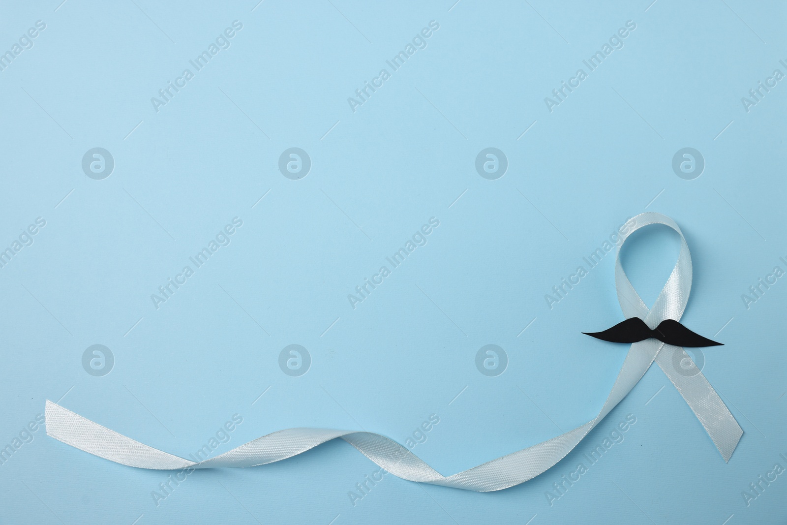 Photo of Light blue ribbon and fake mustache on color background, top view with space for text. Prostate cancer awareness