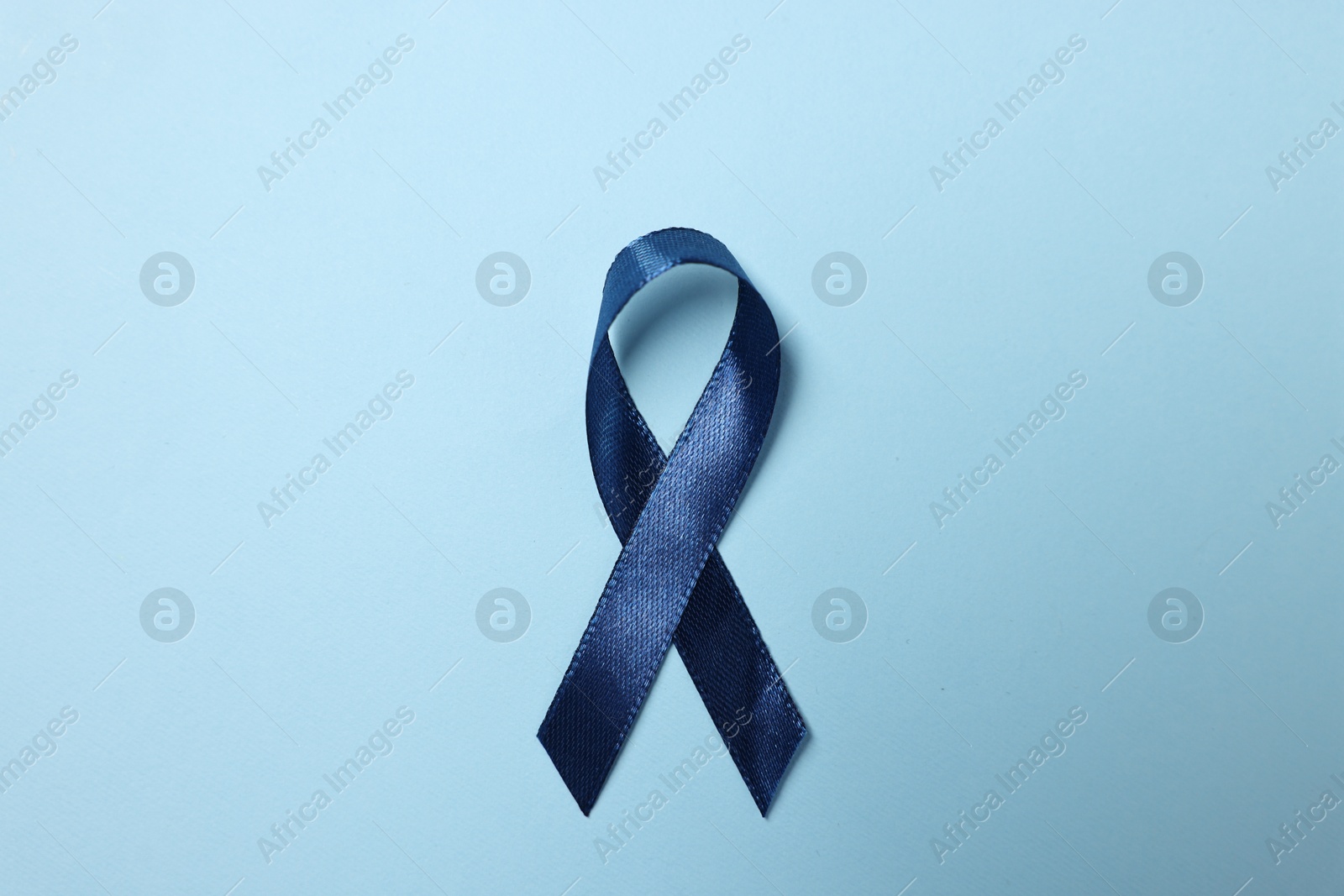 Photo of Dark blue ribbon on color background, top view. Prostate cancer awareness