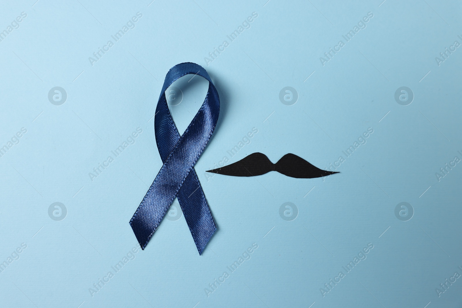 Photo of Dark blue ribbon and fake mustache on color background, top view. Prostate cancer awareness