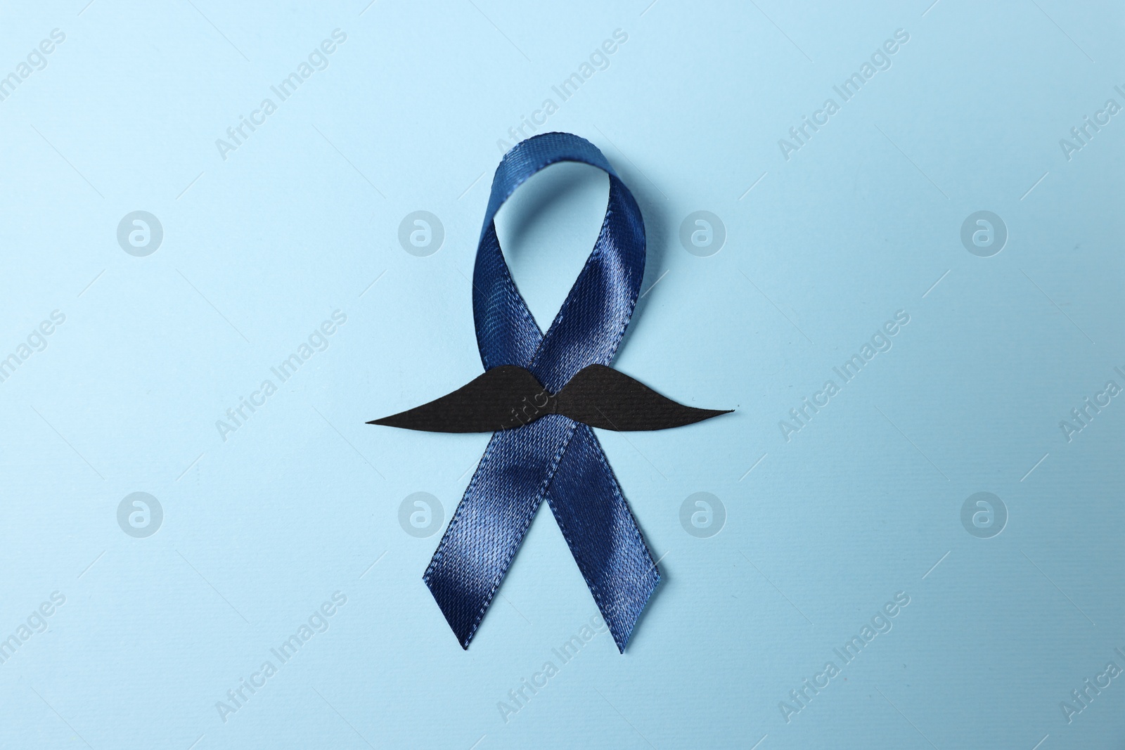 Photo of Dark blue ribbon and fake mustache on color background, top view. Prostate cancer awareness