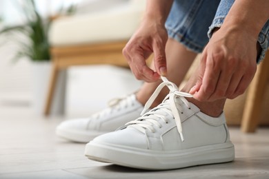 Woman tying shoelace of white sneaker indoors, closeup