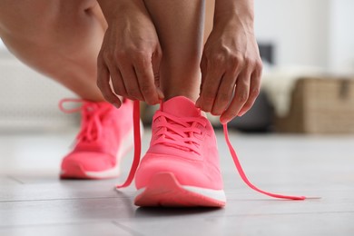 Photo of Woman tying shoelace of pink sneaker indoors, closeup