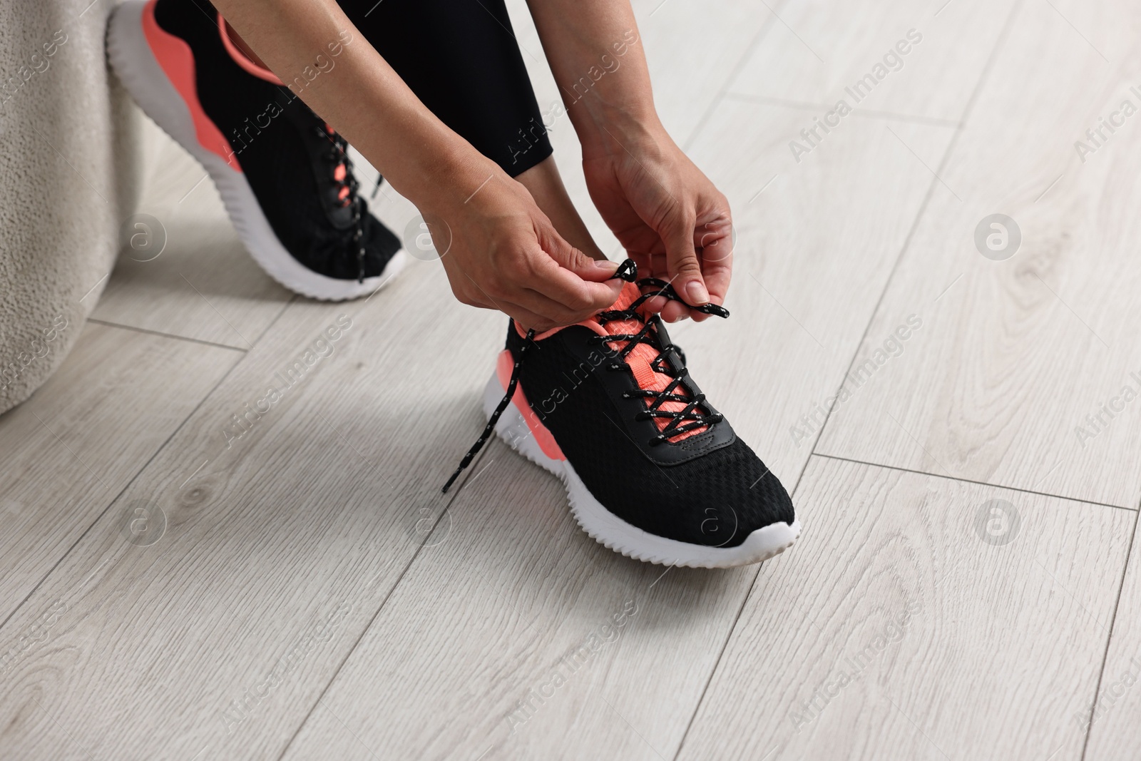 Photo of Woman tying shoelace of sneaker indoors, closeup