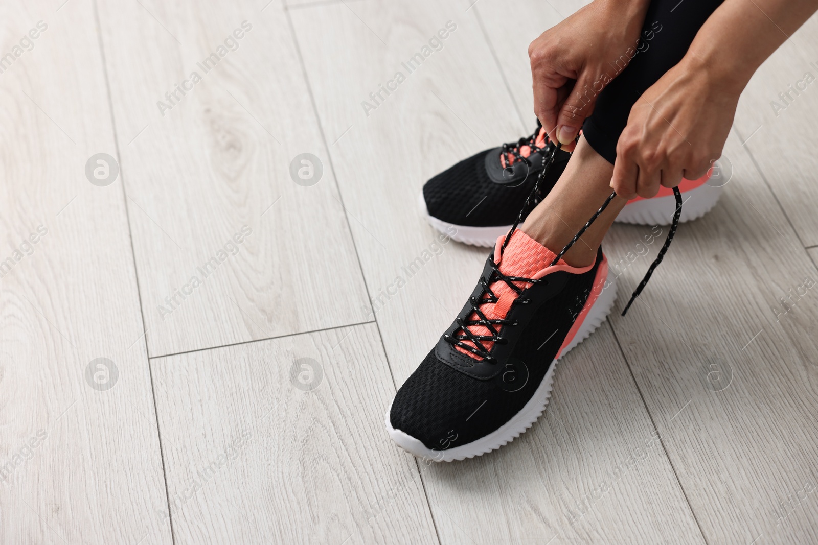 Photo of Woman tying shoelace of sneaker indoors, closeup. Space for text