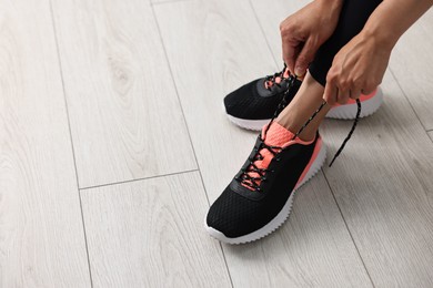 Photo of Woman tying shoelace of sneaker indoors, closeup. Space for text