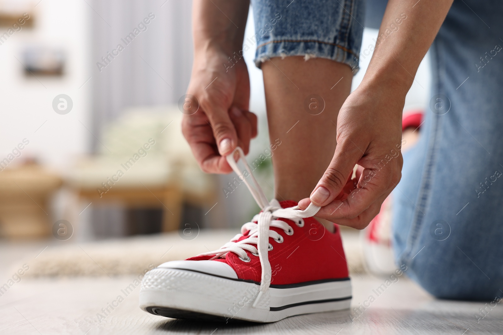 Photo of Woman tying shoelace of red sneaker indoors, closeup