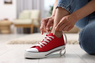 Photo of Woman tying shoelace of red sneaker indoors, closeup