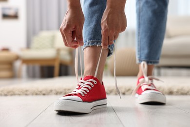 Photo of Woman tying shoelace of red sneaker indoors, closeup