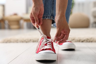 Photo of Woman tying shoelace of red sneaker indoors, closeup