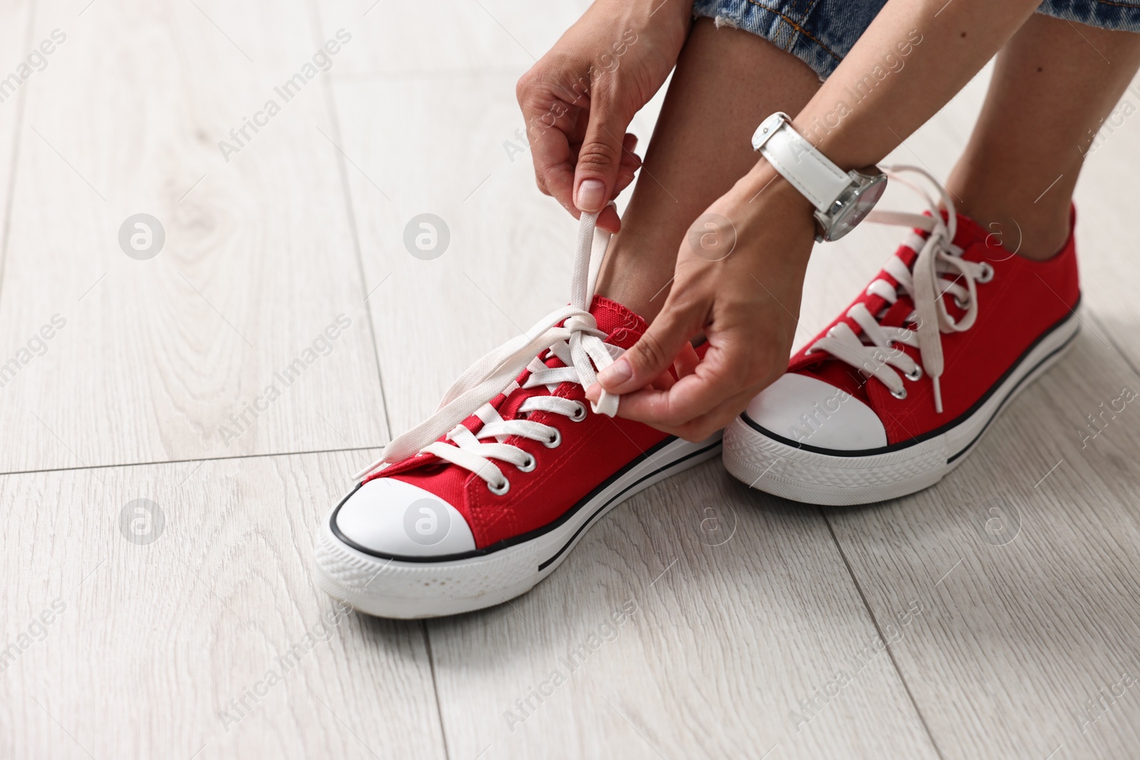 Photo of Woman tying shoelace of red sneaker indoors, closeup