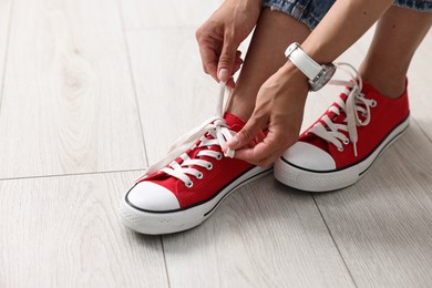 Photo of Woman tying shoelace of red sneaker indoors, closeup