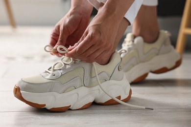 Photo of Woman tying shoelace of sneaker indoors, closeup