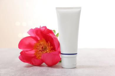 Photo of Tube of cosmetic product and peony flower on gray table against light background