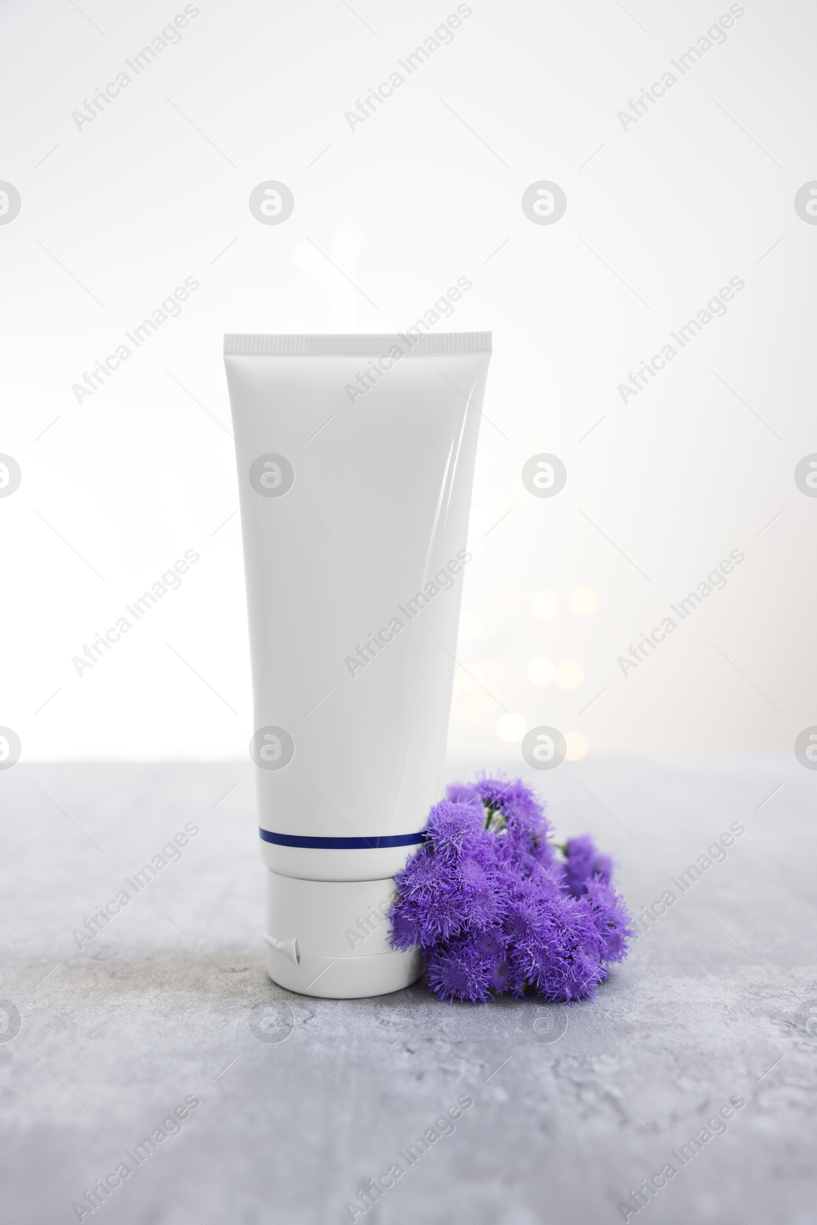 Photo of Tube of cosmetic product and ageratum flowers on gray table against light background