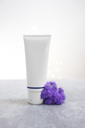 Photo of Tube of cosmetic product and ageratum flowers on gray table against light background