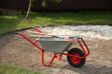 Photo of Wheelbarrow with rake and shovel outdoors. Gardening tools