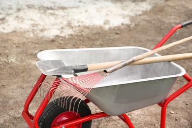 Wheelbarrow with rake and shovel outdoors. Gardening tools