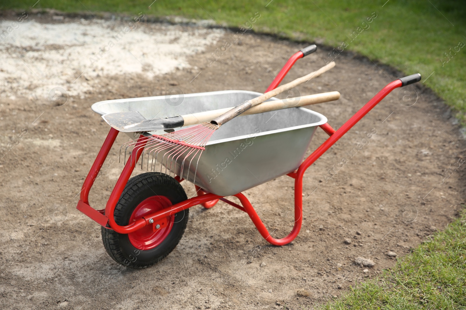 Photo of Wheelbarrow with rake and shovel outdoors. Gardening tools