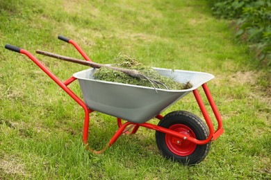 Photo of Wheelbarrow with mown grass and pitchfork outdoors